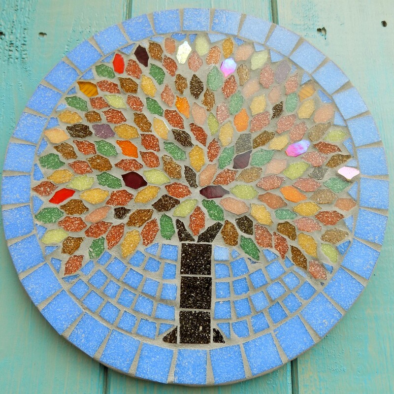 A unique  mosaic garden hanging plaque with a tree design using the rich colours of autumn in the leaves on a sky blue background