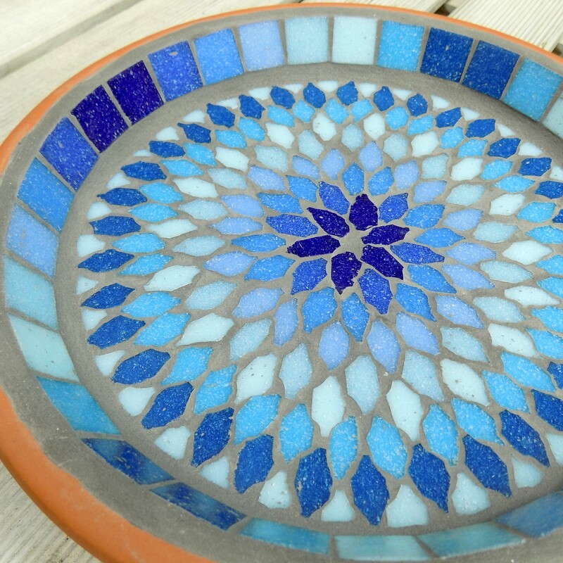 A mosaic birdbath with a mandala style design made with shades of blues and turquoise tiles