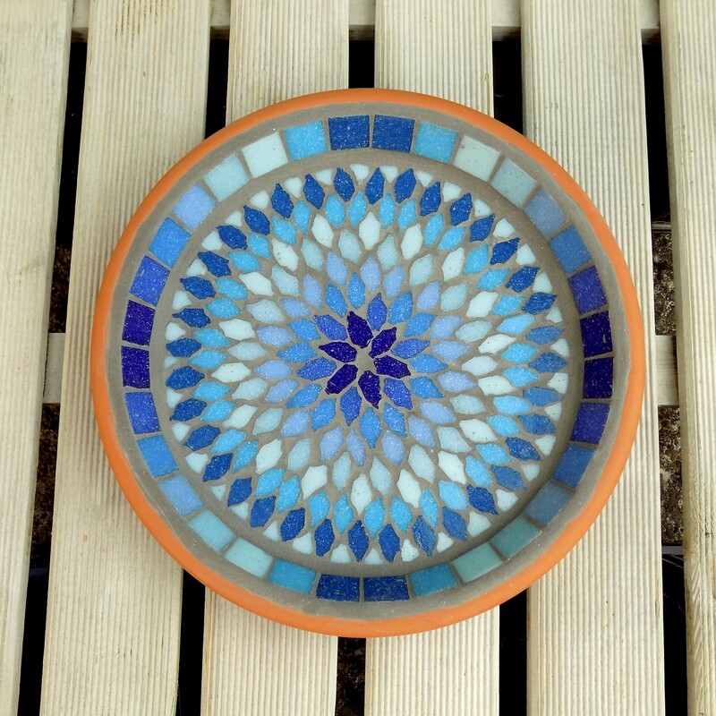 A mosaic garden bird bath with a mandala style design made with shades of blues and turquoise tiles
