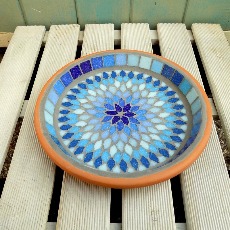 A mosaic garden birdbath with a mandala style design made with shades of blues and turquoise tiles
