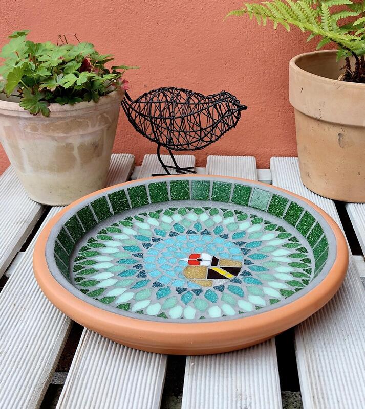 A mosaic birdbath with a design of a goldfinch bird in the centre of a splash effect of green tiles