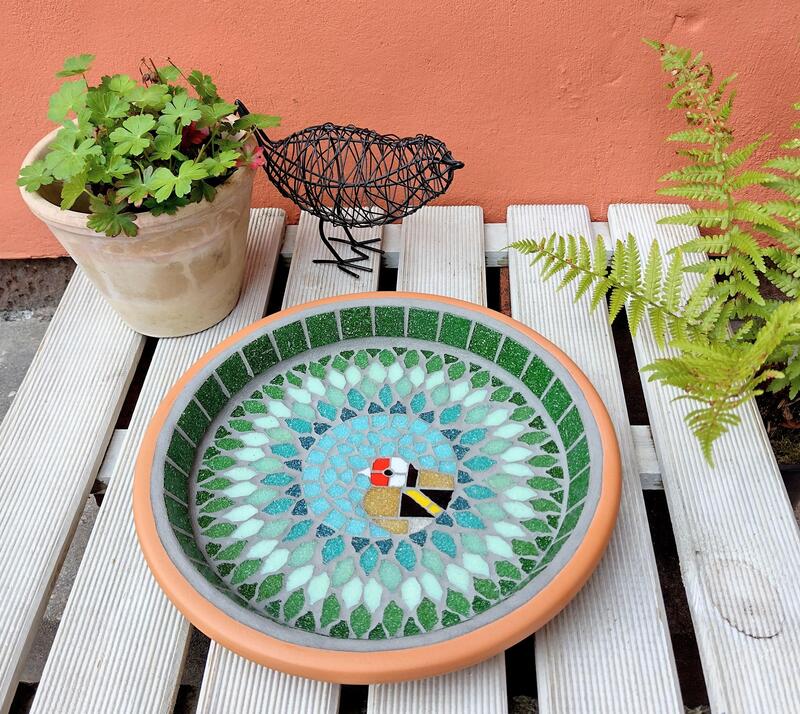 A mosaic garden birdbath with a design of a goldfinch bird in the centre of a splash effect of green tiles