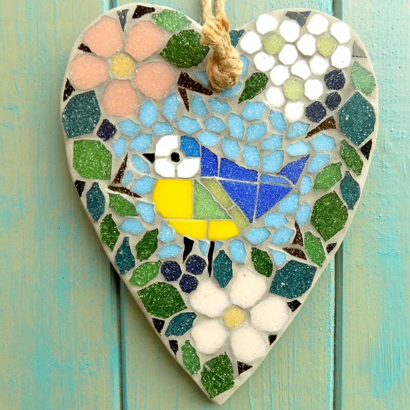 A handmade mosaic hanging heart with a design of a bluetit bird standing surrounded by a border of hedgerow leaves and flowers