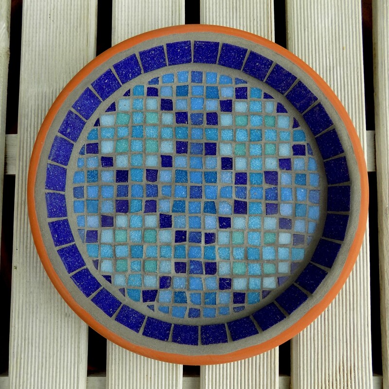 A mosaic bird bath with a design inspired by a Moroccan pool with shades of blue tiles creating a geometric pattern