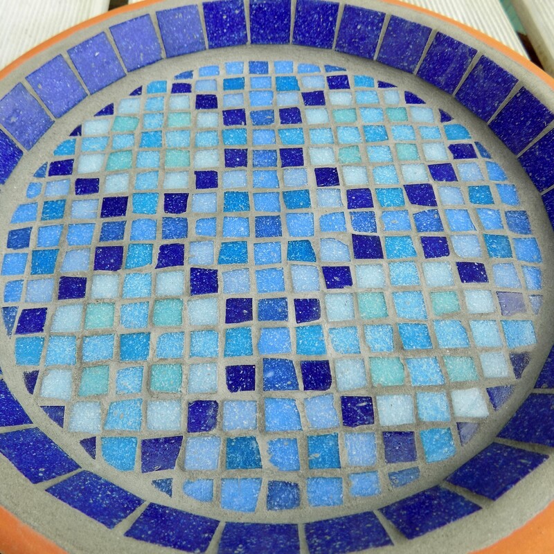 A mosaic birdbath with a design inspired by a Moroccan pool with shades of blue tiles creating a geometric pattern