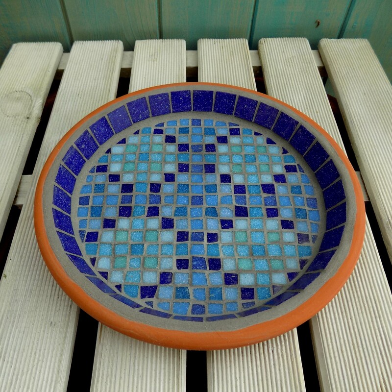 A mosaic garden bird bath with a design inspired by a Moroccan pool with shades of blue tiles creating a geometric pattern