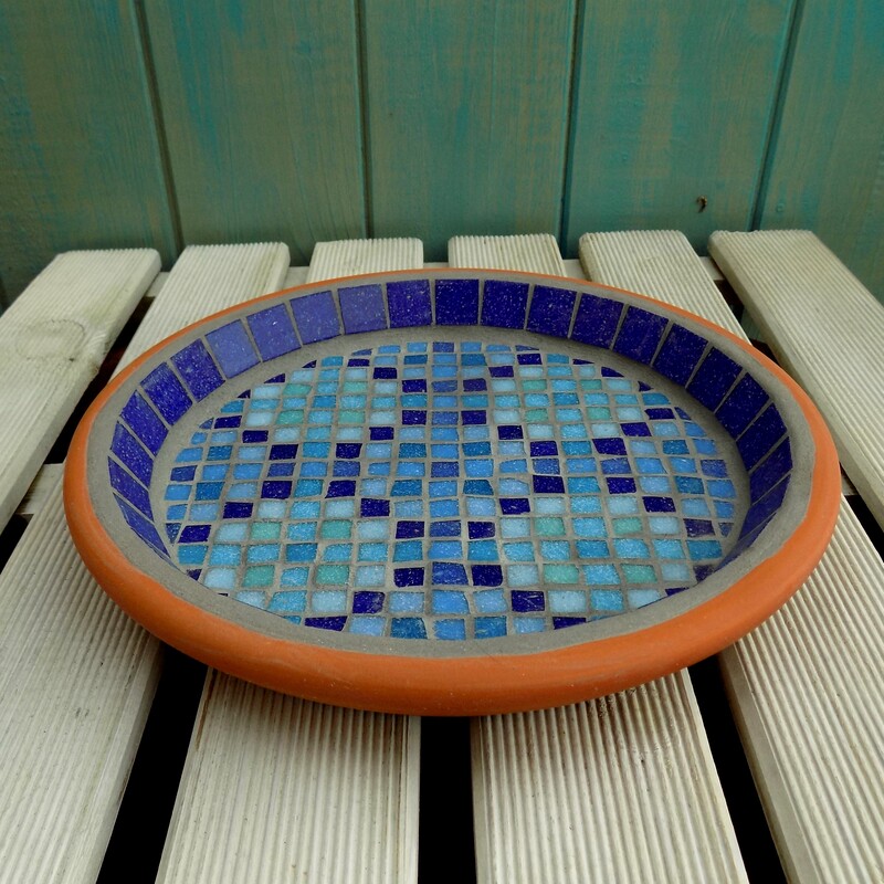 A mosaic garden birdbath with a design inspired by a Moroccan pool with shades of blue tiles creating a geometric pattern