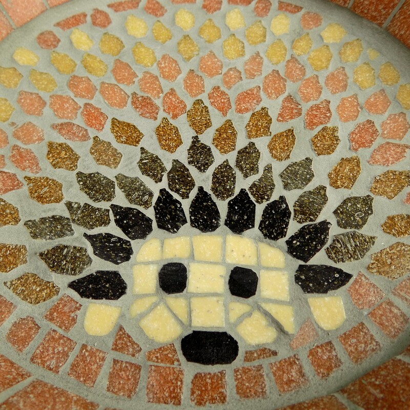 A mosaic bird bath with a design of a hedgehog made with shades of brown