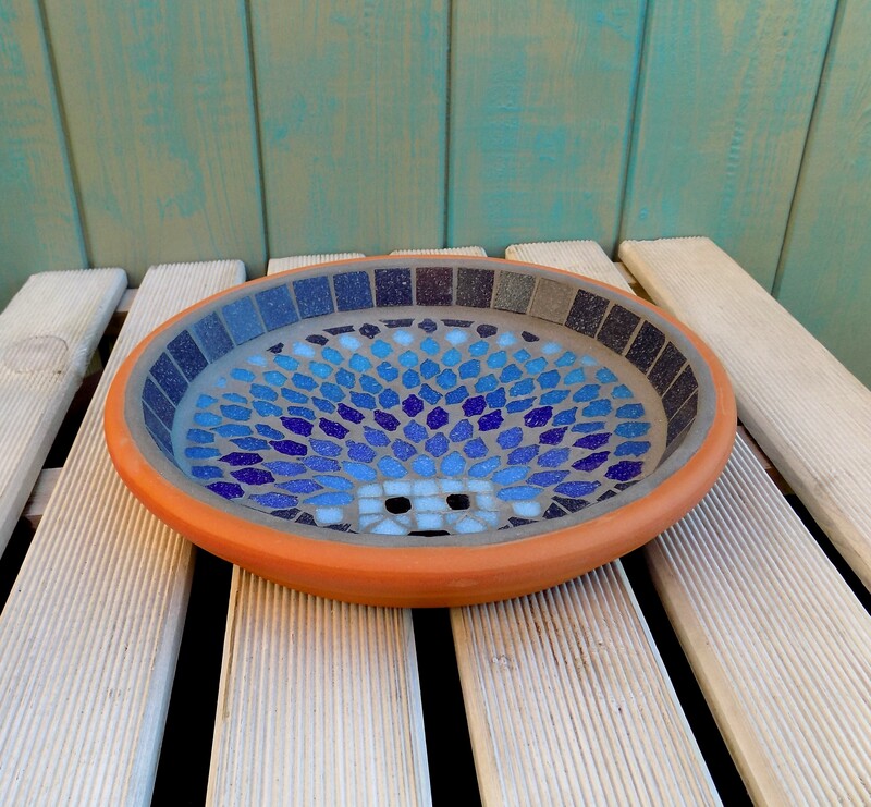A mosaic birdbath with a design of  a hedgehog made in shades of blues with a deep navy background
