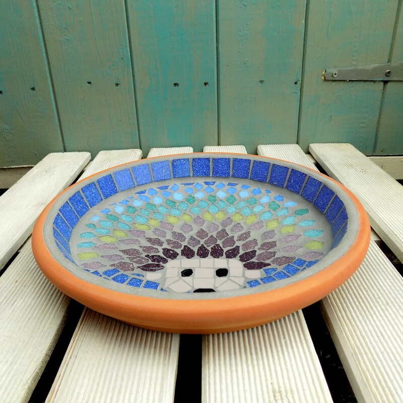 A mosaic birdbath with a design of a hedgehog with each line of spines made in a rainbow of tile colours 