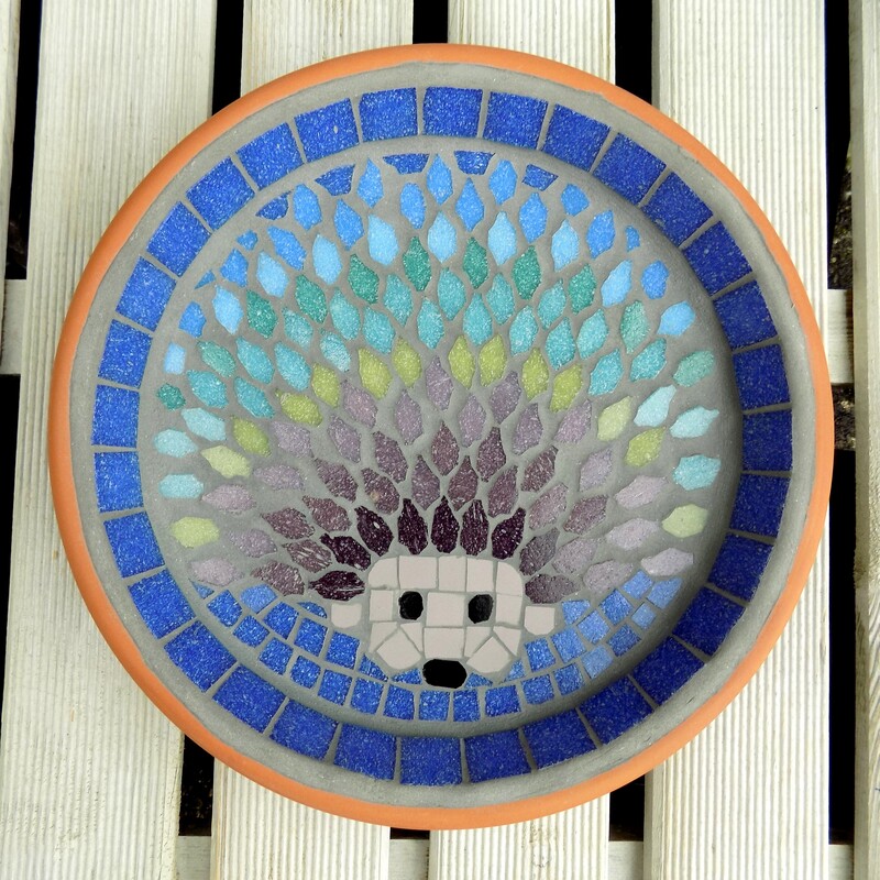 A mosaic garden  birdbath with a design of a hedgehog with each line of spines made in a rainbow of tile colours 