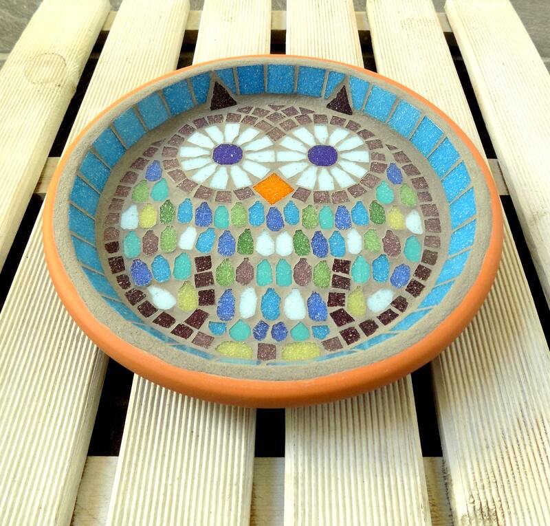 A mosaic bird bath with a design of a colourful owl in turquoise, purples, greens and blue tiles