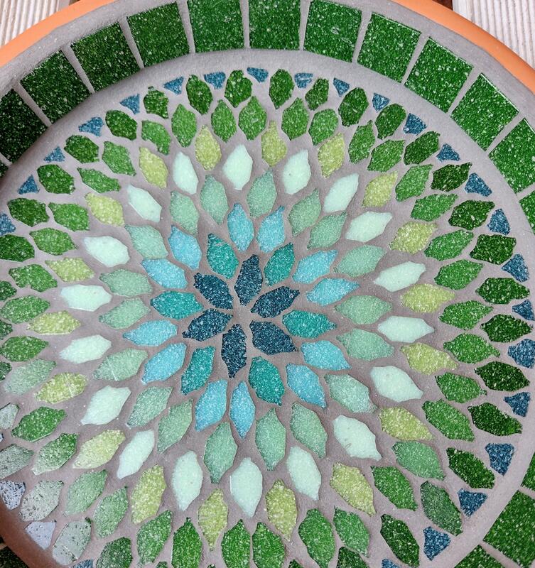 A mosaic garden bird bath with a mandala style design in shades of greens