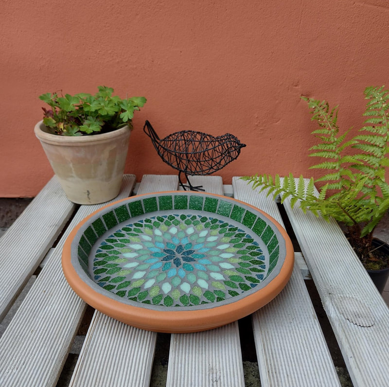 A mosaic garden birdbath with a mandala style design in shades of greens