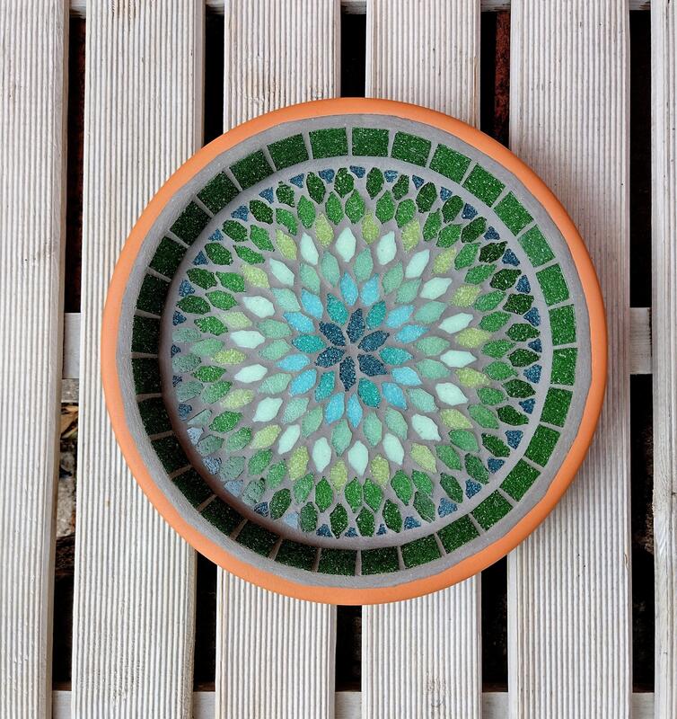 A mosaic birdbath with a mandala style design in shades of greens