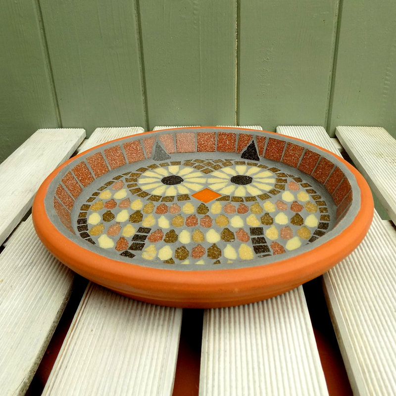 A mosaic birdbath with a design of a tawny owl made with browns, terracotta and cream tiles.