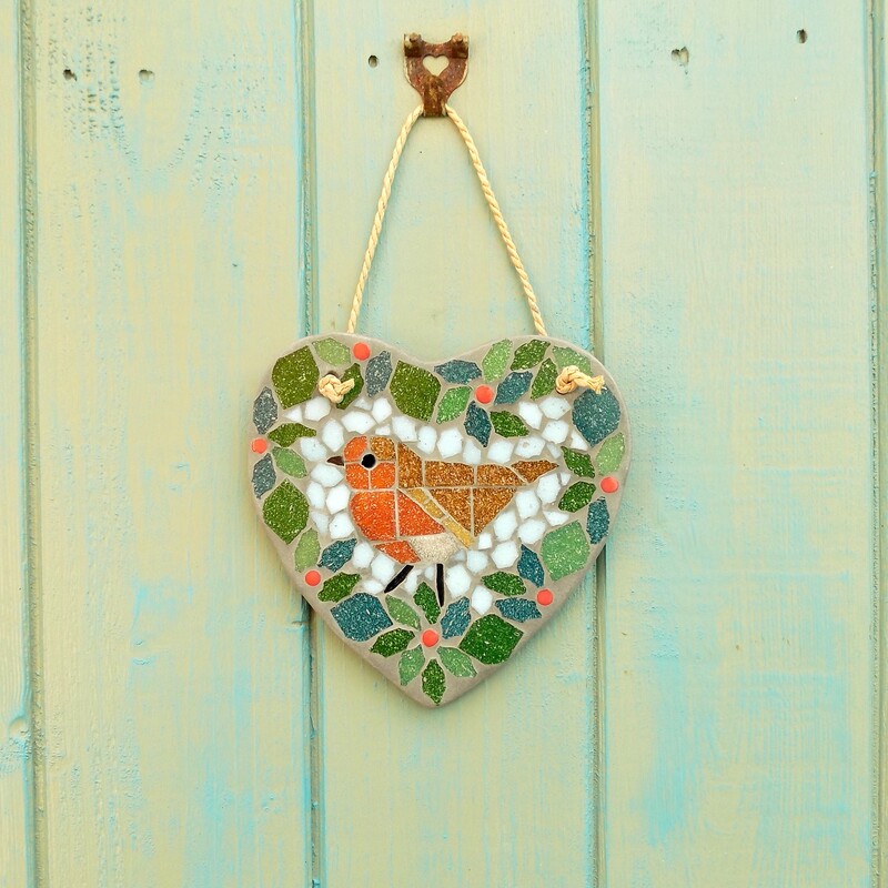 A mosaic hanging heart with a design of a robin bird standing in the centre of a foliage wreath with red berries