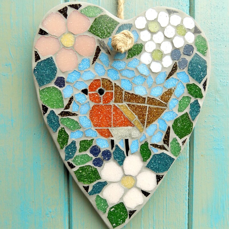 A mosaic hanging heart with a design of a robin standing in a border of hedgerow leaves and flowers