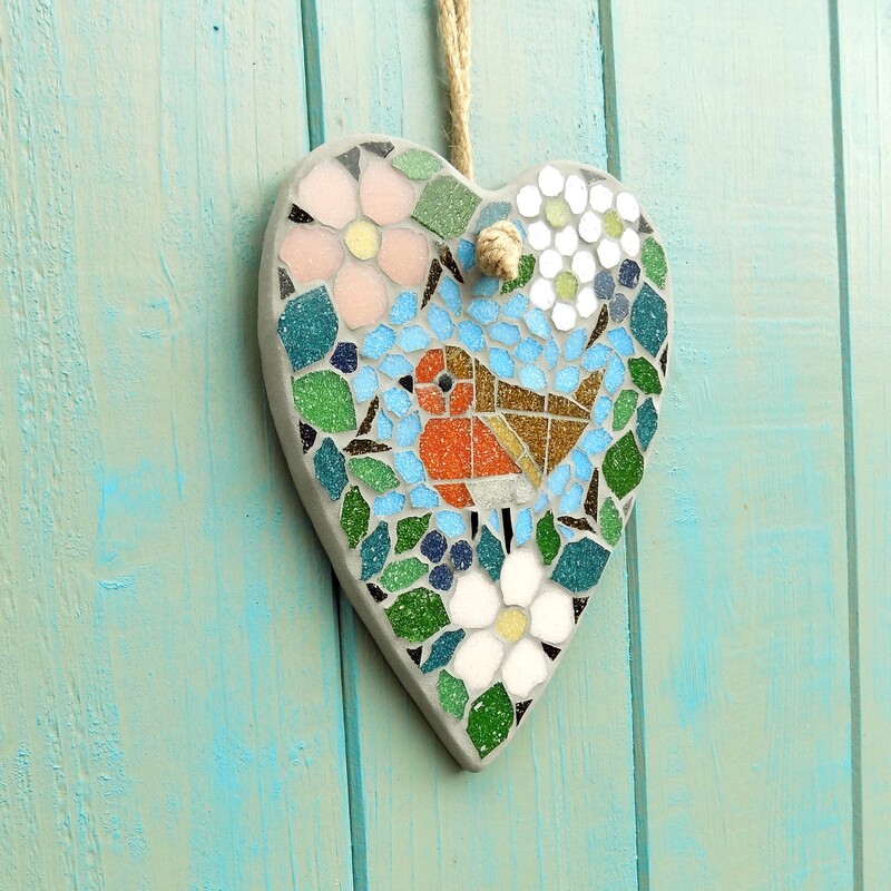 A mosaic garden hanging heart with a design of a robin standing in a border of hedgerow leaves and flowers