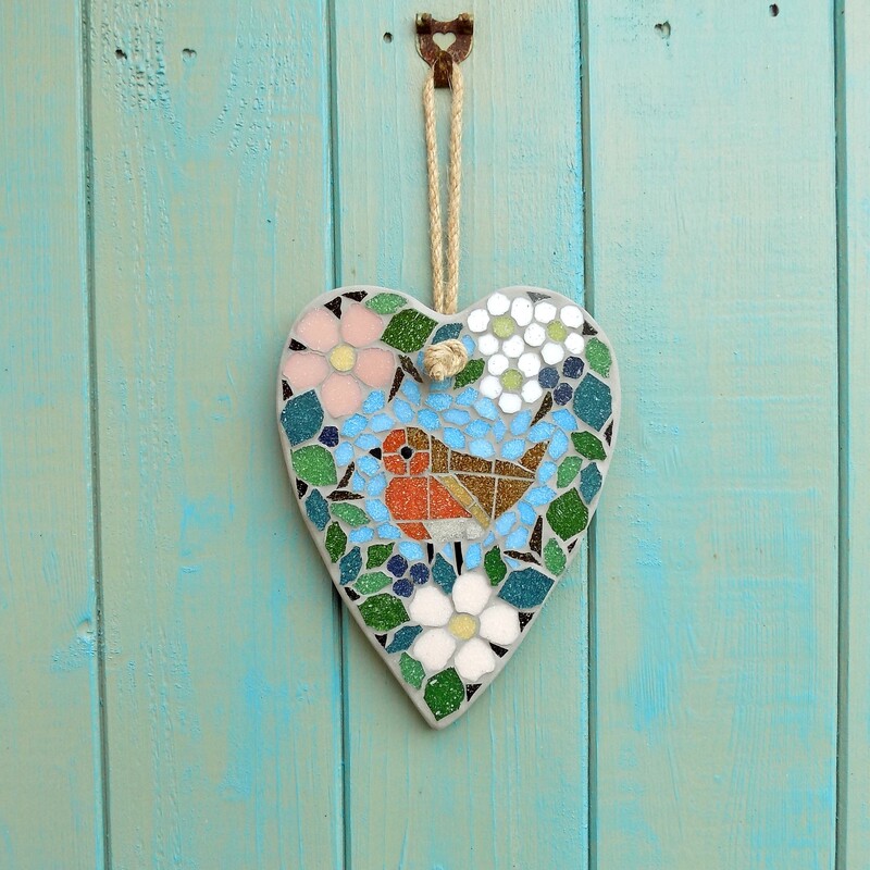 A handmade mosaic hanging heart with a design of a robin standing in a border of hedgerow leaves and flowers