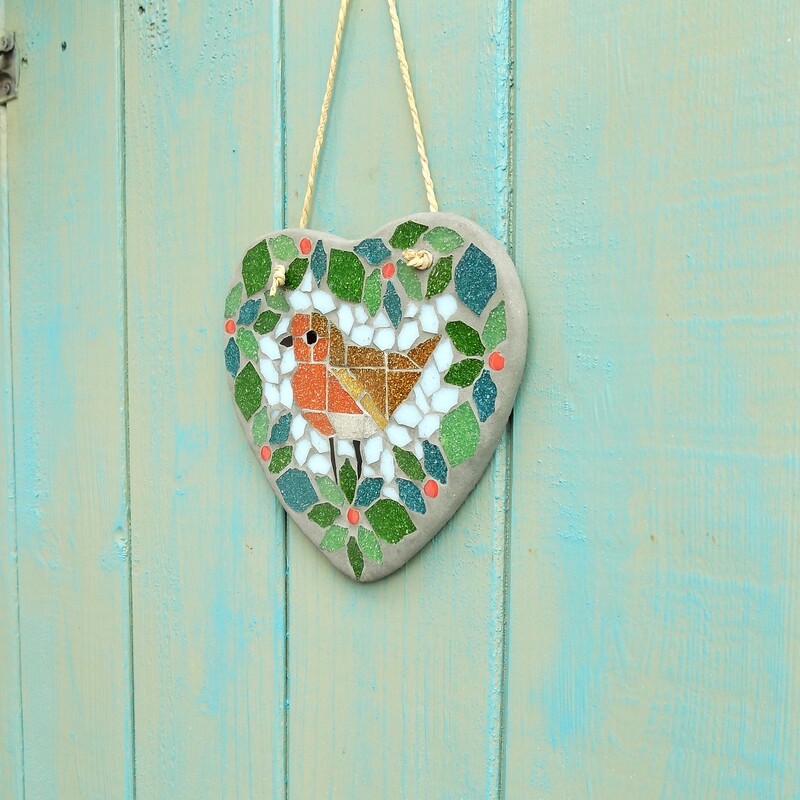 A handmade mosaic hanging heart with a design of a robin bird standing in the centre of a foliage wreath with red berries