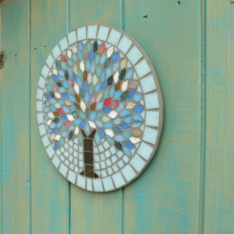A hanging garden mosaic plaque with a tree reflecting the colours of winter in it's leaves on a pale aqua background
