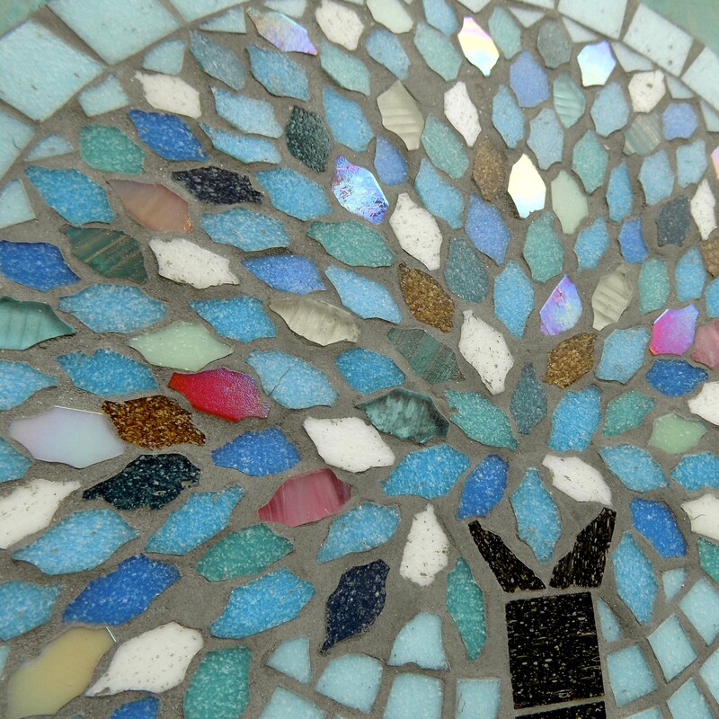 A mosaic hanging garden plaque with a tree reflecting the colours of winter in it's leaves on a pale aqua background